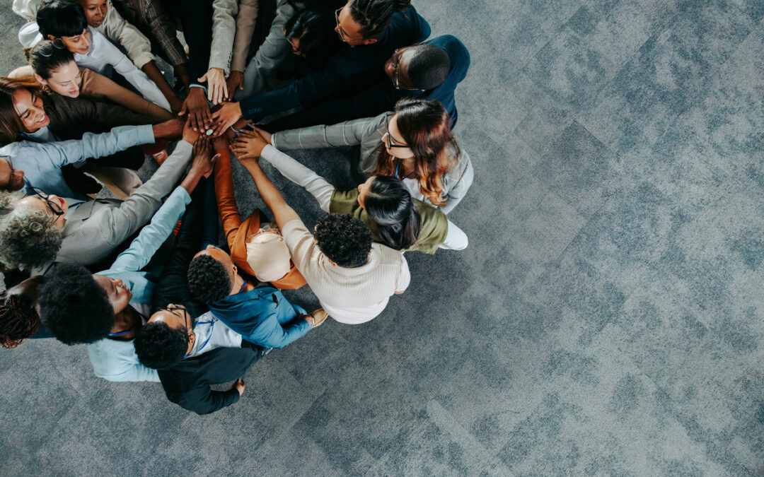 Clinical studies blog. The Importance of Diversity in Clinical Trial Recruitment: this photograph shows a diverse group of individuals coming together in a circle with their hands together.