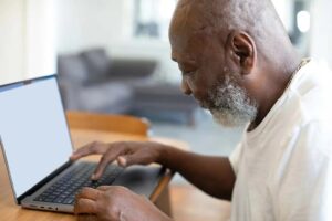 A man types on a laptop. This post looks at decentralized clinical trials and considers the pros and cons. Clinical studies blog.